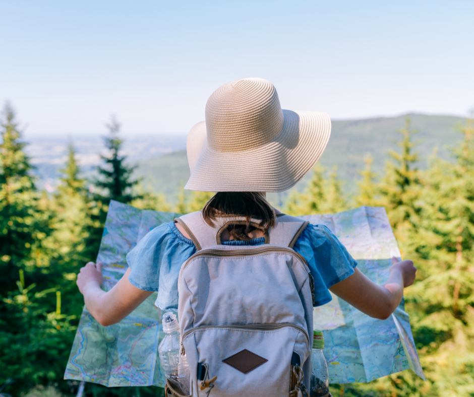 Zdjęcie przedstawia kobietę z plecakiem trzymająca mapę na tle wysokich drzew