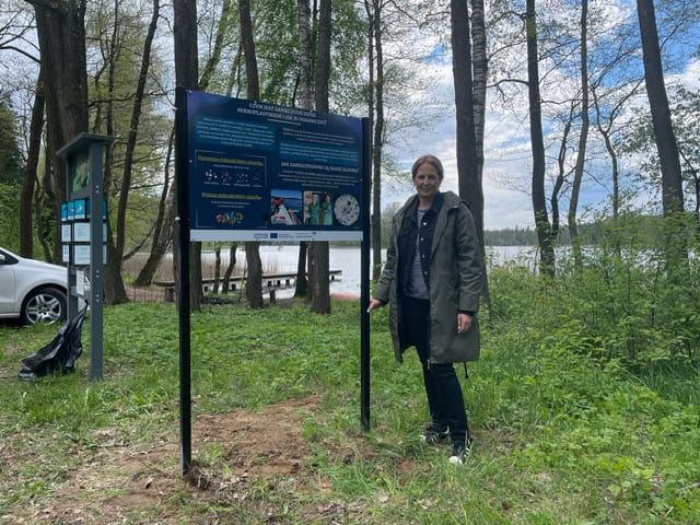 Magdalena Jurgielewicz z Fundacji Ochrony Wielkich Jezior Mazurskich przy plakacie przy jeziorze w Jakunówku