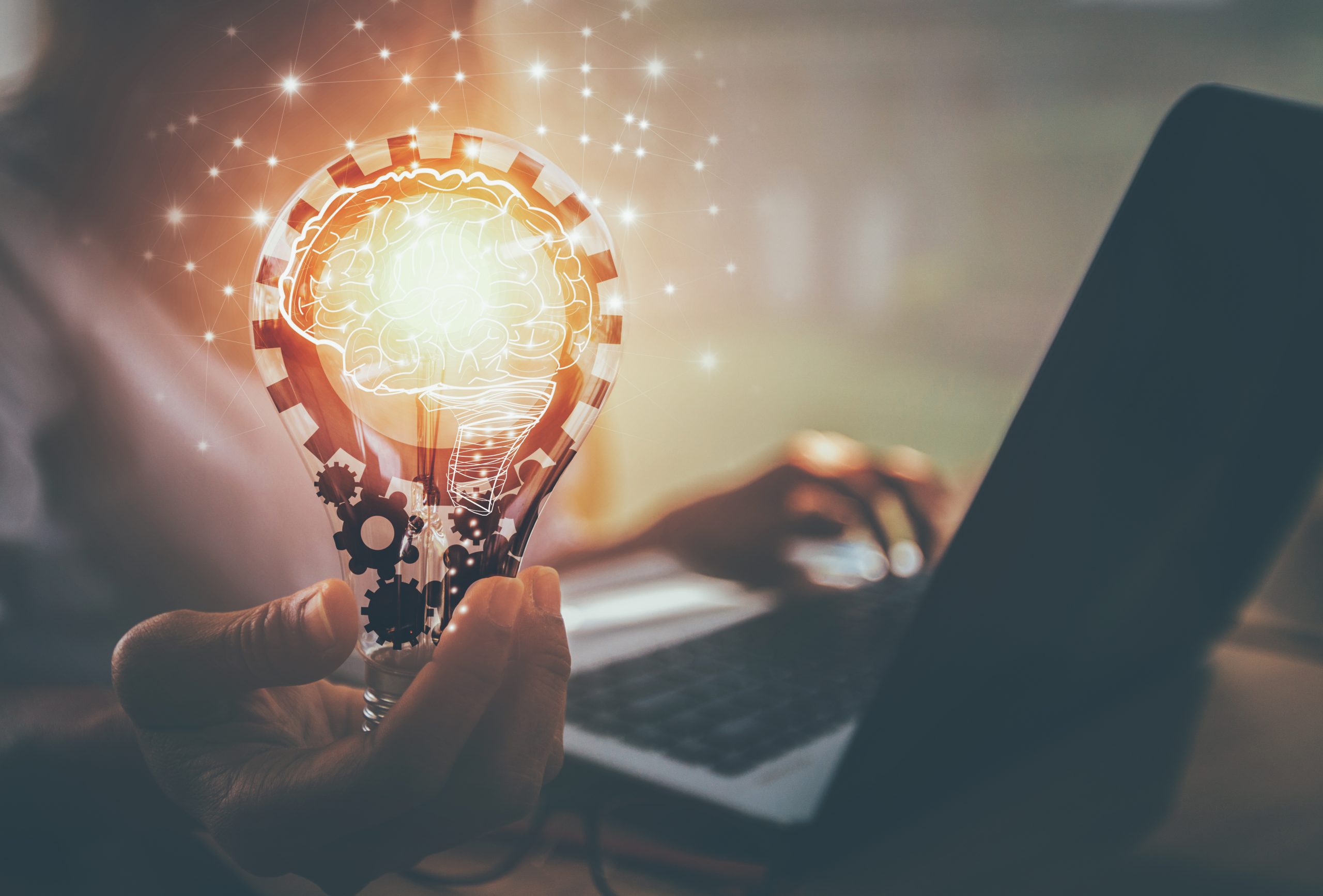 Kobieta pracuje na laptopie, trzyma zapaloną żarówkę w ręku