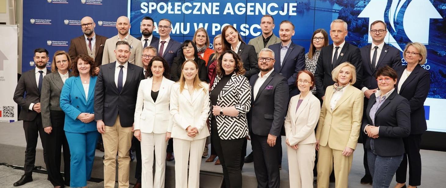 Fotografia przedstawia ok. 25 osób. Zdjęcie zostało wykonane na tle z napisem \