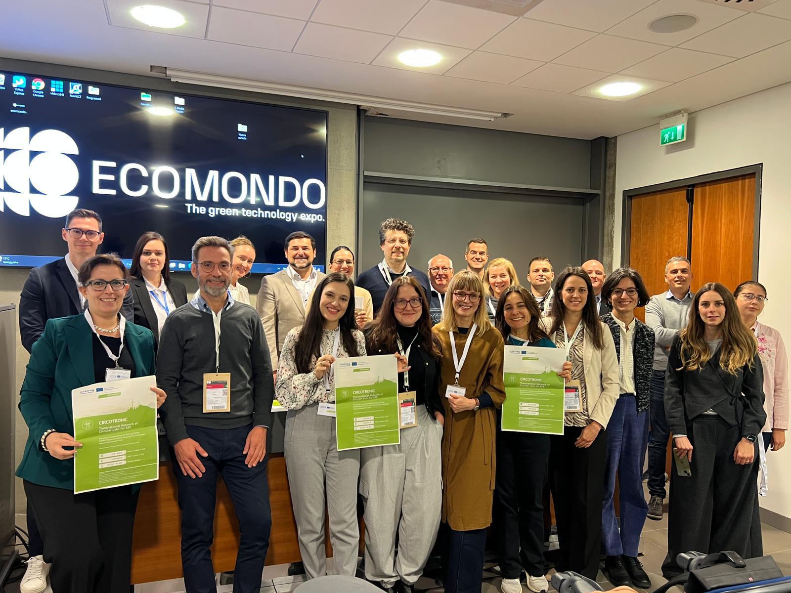 Zdjęcie uczestników konferencji finałowej trzymających plakaty projektowe na tle nazwy projektu