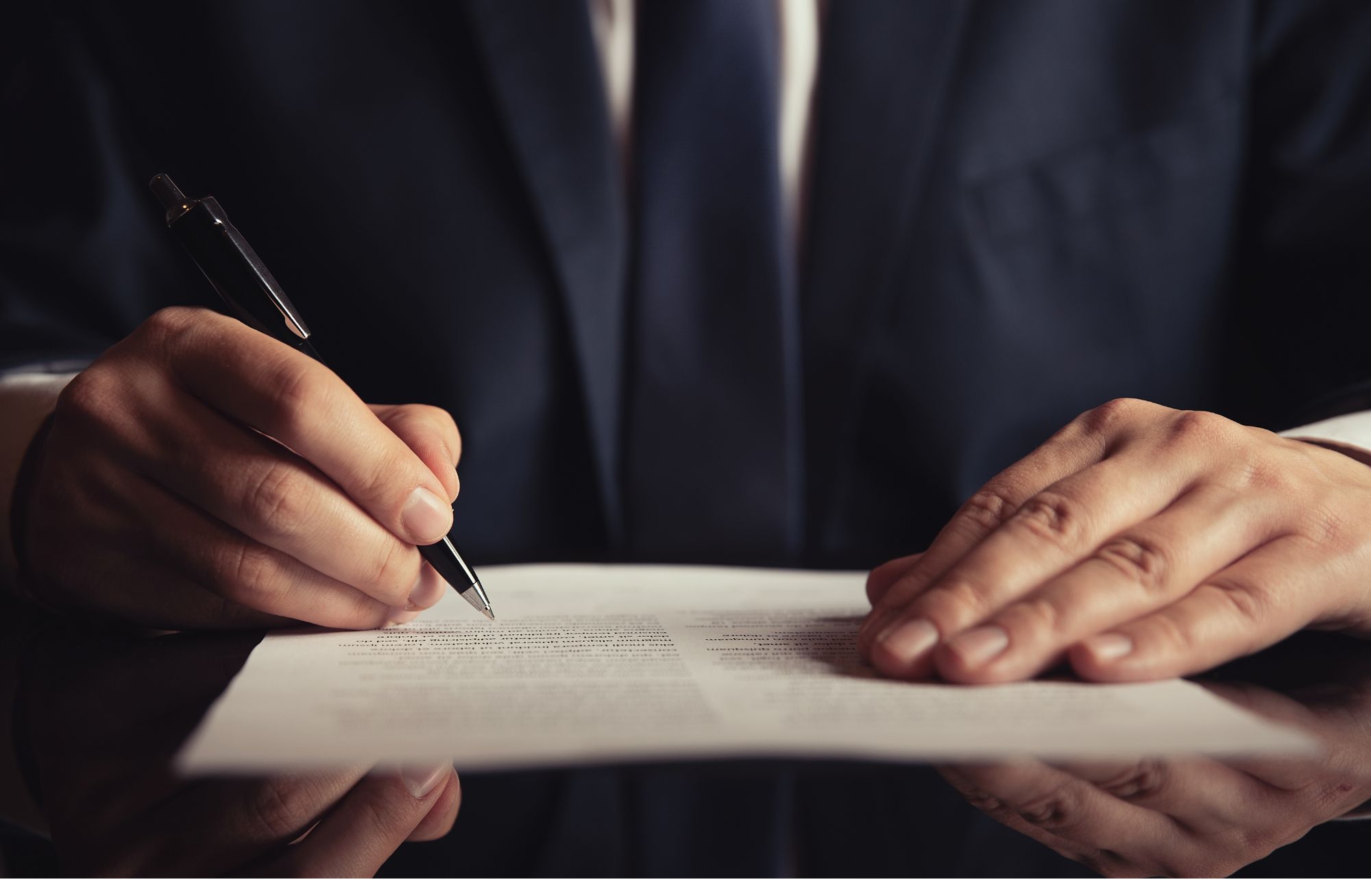 Zdjęcie poglądowe do informacji o podpisaniu umowy. na zdjęciu dłonie, w jednej ręce długopis nad kartką papieru.